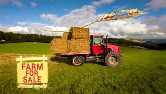 In the background, there are rolling fields of green farmland below a blue sky. In the mid-ground, a red tractor is hauling hay bales. Above the tractor, there is a strand of wheat with 'APR' written on it. In the foreground, there is a palette holding a sign stating 'Farm For Sale' in red.